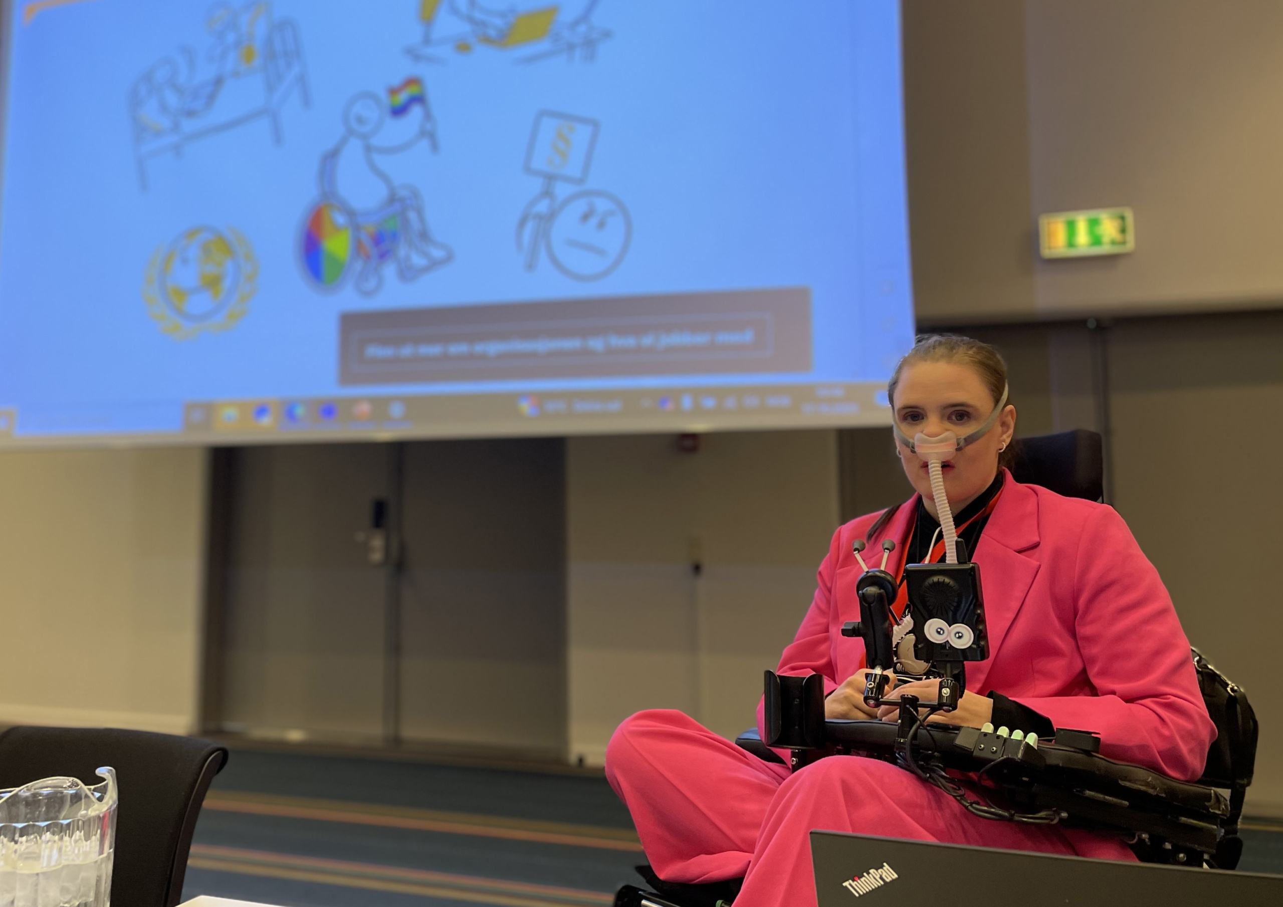 Ingrid Thunem dresssed in bright pink clothes giving a speech sitting in a wheelchair. 