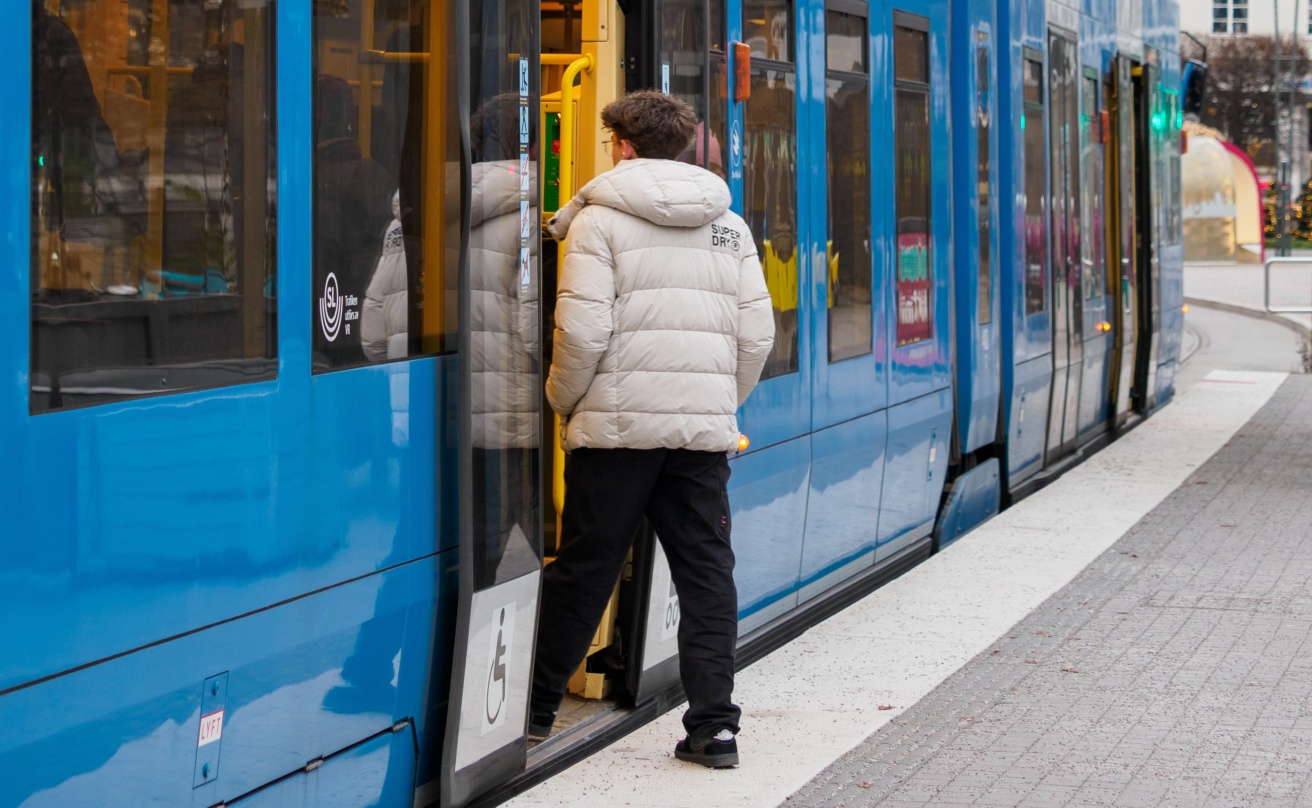 Ung man stiger på Tvärbanan i Stockholm. Snabbspårvagnen är tillgänglig och har lågt golv.