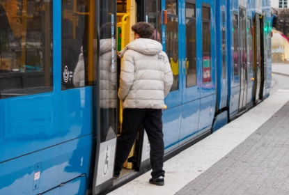Ung man stiger på Tvärbanan i Stockholm. Snabbspårvagnen är tillgänglig och har lågt golv.