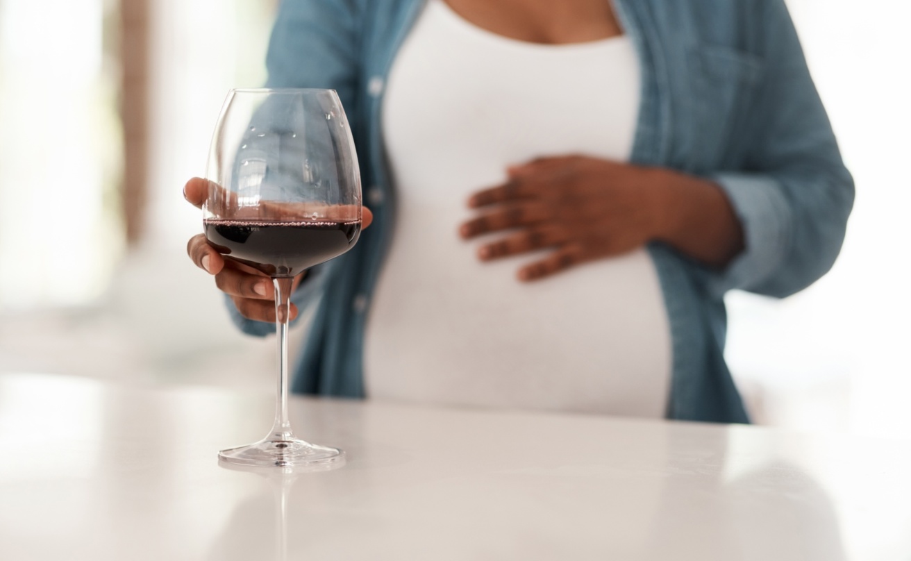 Pregnant women reaching out for a glass of red wine