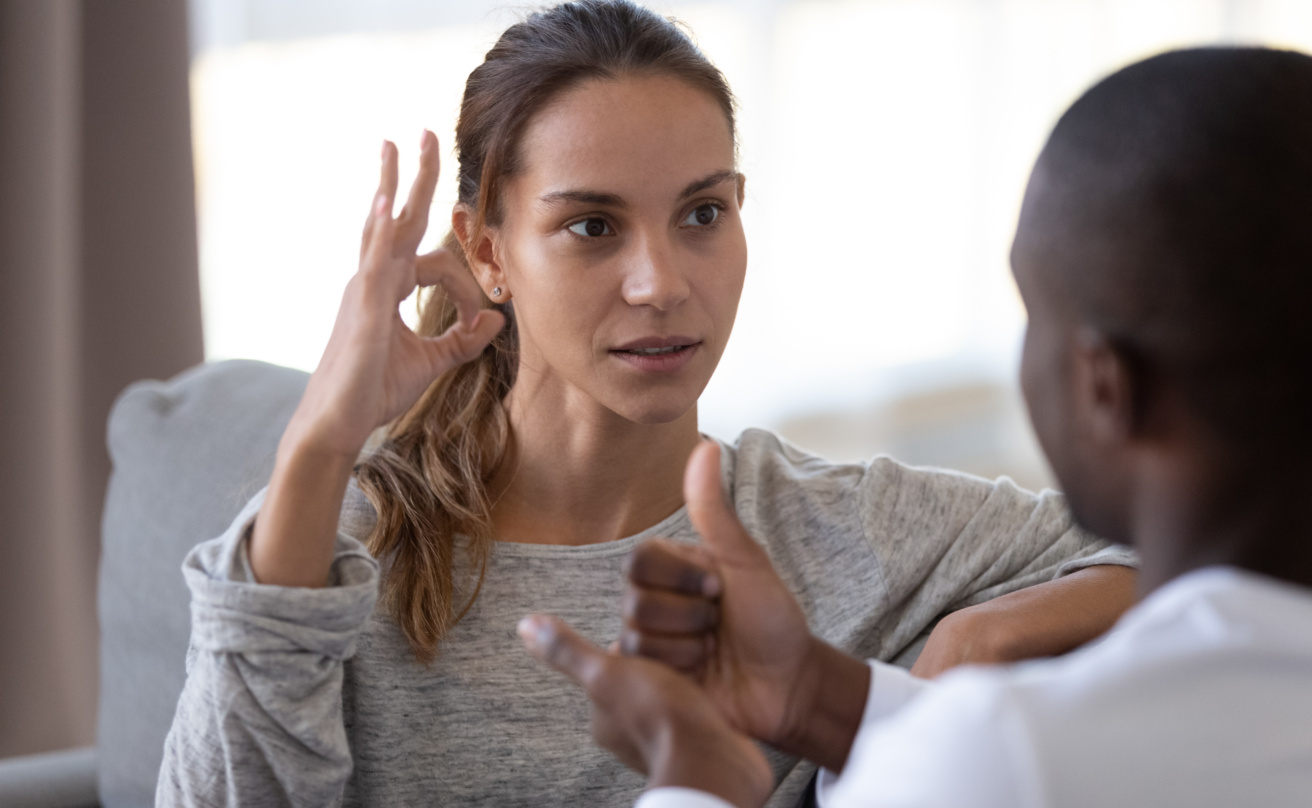 Woman signing OK in sign language to a man sitting opposite her.
