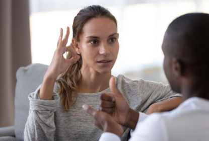 Woman signing OK in sign language to a man sitting opposite her.
