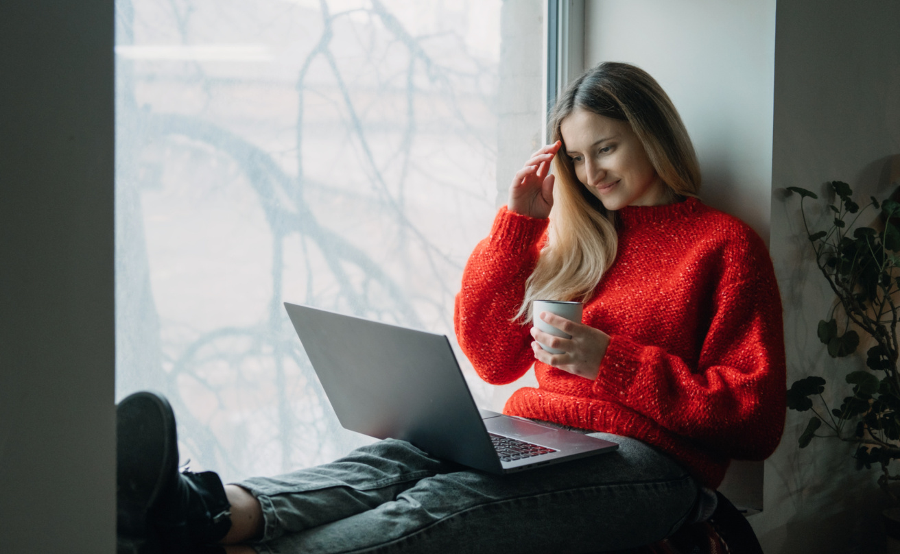 Woman with red shirt looking at her laptop while smiling