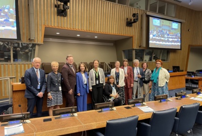 11 people in a conference room at the Nordic side event, posing for a group picture. One woman sitting in a wheelchair, one man holding a white cane