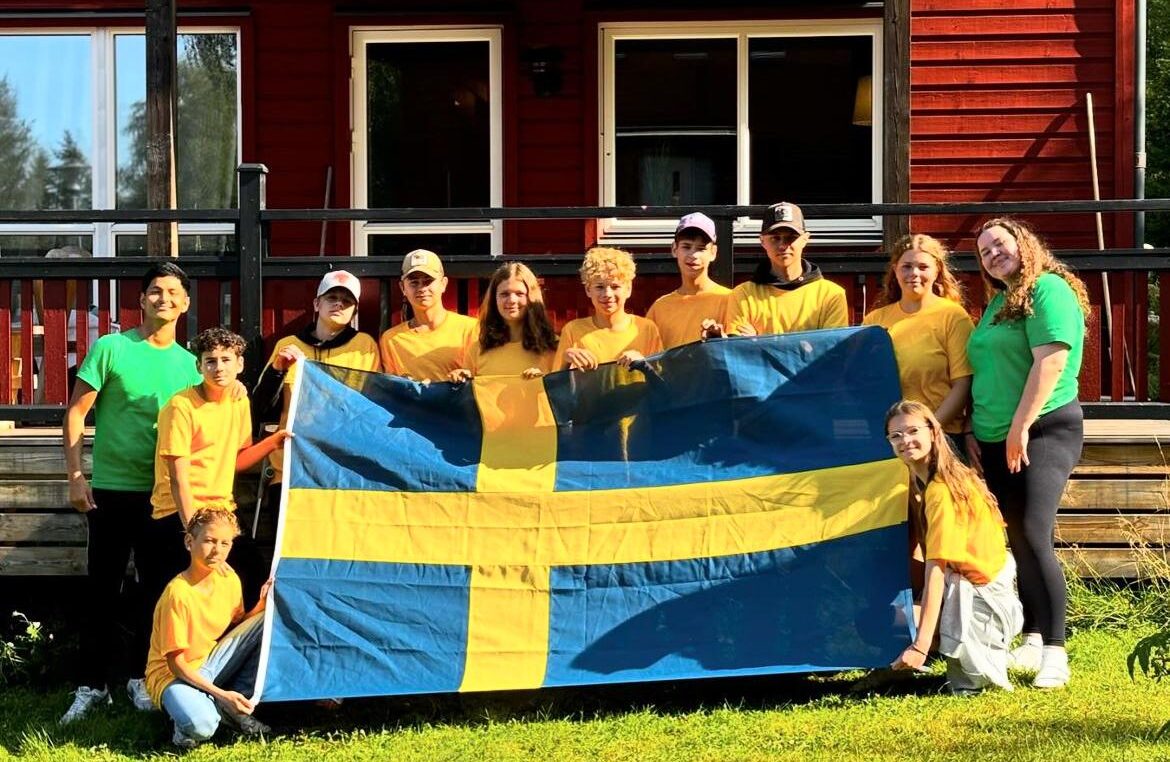 10 camp participants togeher with 2 leaders outside, holding a bilg swedish flag