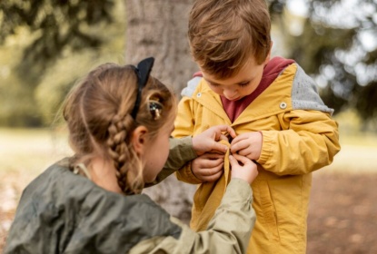 Girl helping boy buttoning jacket.