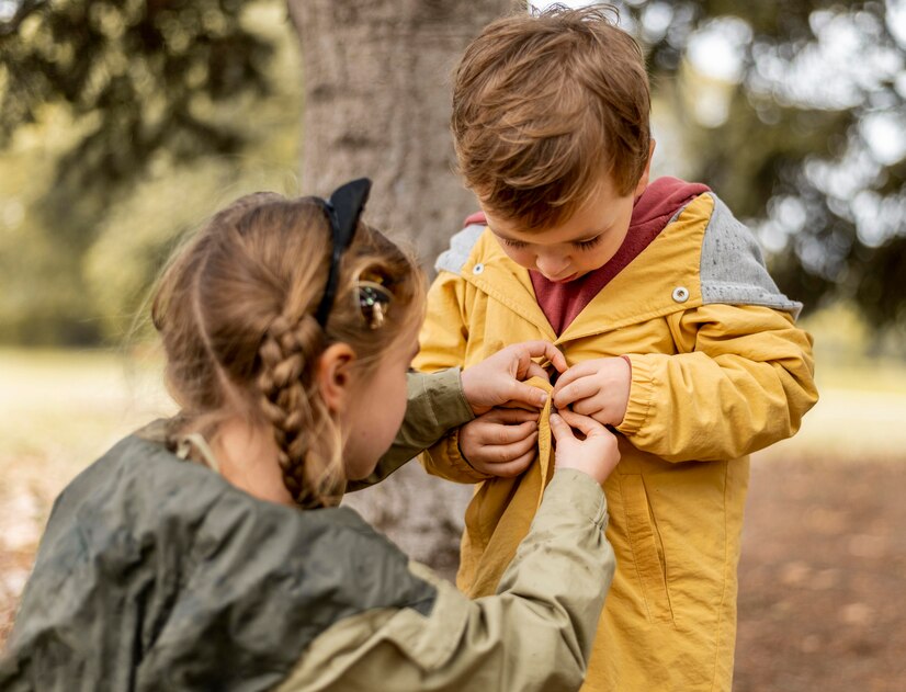 Girl helping boy buttoning jacket.