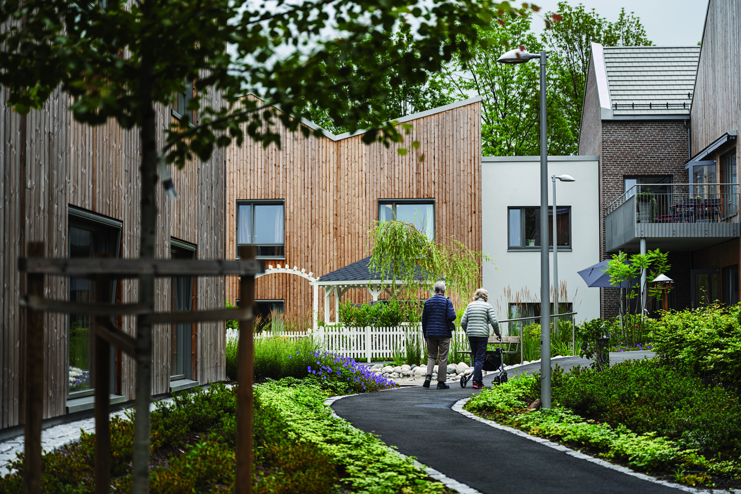 A look inte the Carpe diem dementia village. Two older adults walking on path through green space.