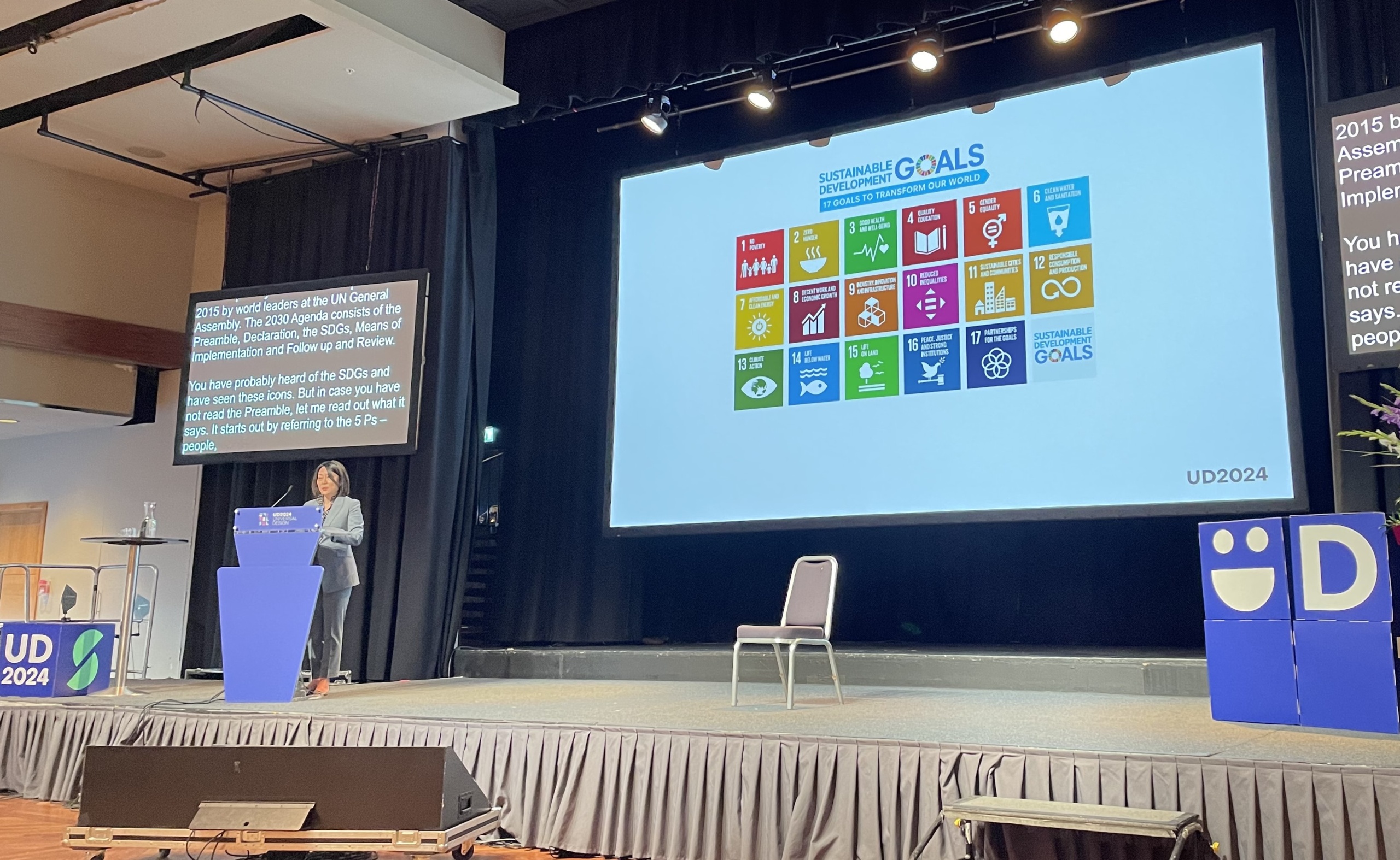 Masumi Ono giving a speech on stage. Picture in the background showing UN headquarters decorated with SDG-coloured lights.