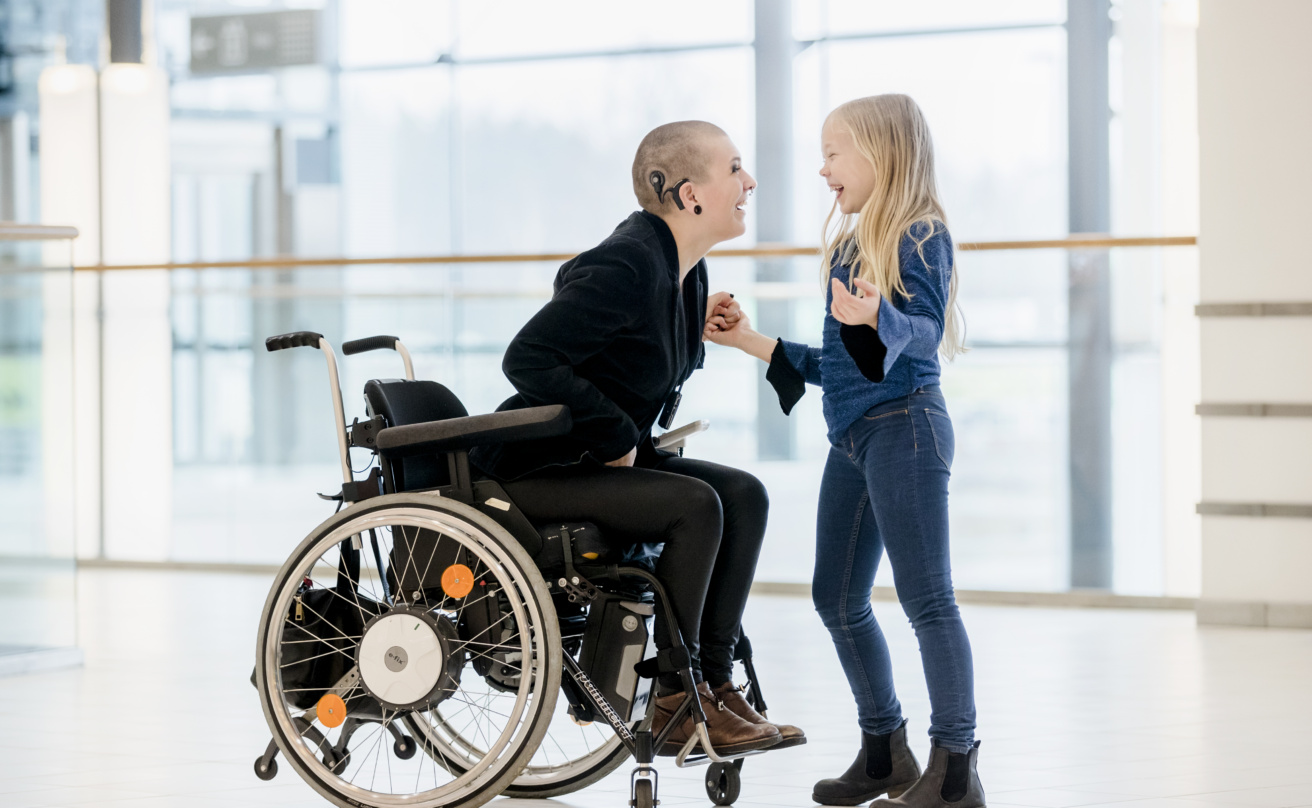 Woman with deafblindness sitting in wheelchair and having a cochlear implant jokes with her daughter