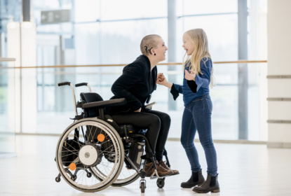 Woman with deafblindness sitting in wheelchair and having a cochlear implant jokes with her daughter