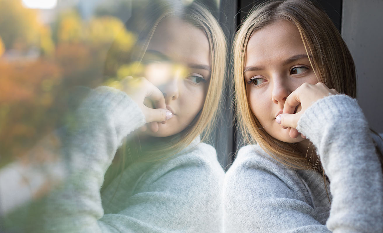 Young woman is sitting by a window, looking out.