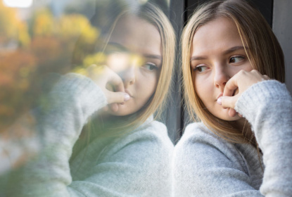 Young woman is sitting by a window, looking out.