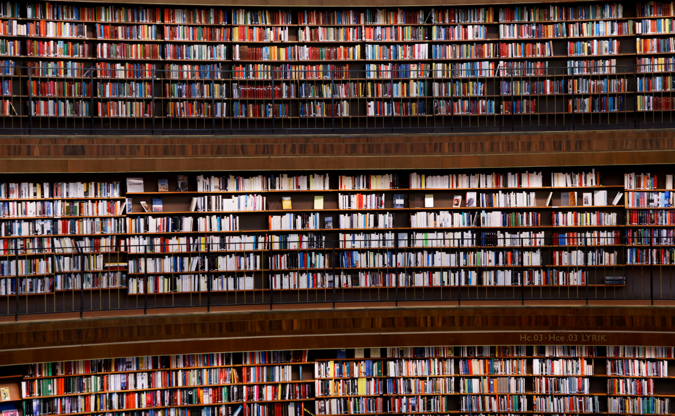 Interior of Stockholm Public Library featuring tall, curved bookshelves filled with books in various colours. The shelves extend across several levels with balconies and dark railings.