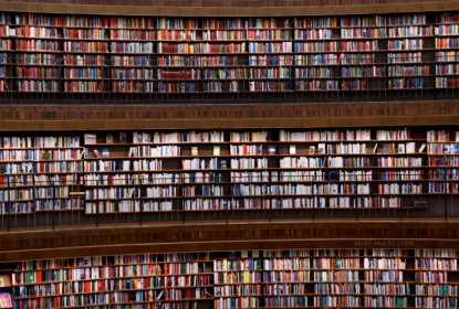 Interior of Stockholm Public Library featuring tall, curved bookshelves filled with books in various colours. The shelves extend across several levels with balconies and dark railings.
