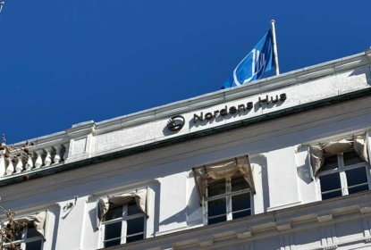 Facade of Nordens Hus with the Nordic Council flag waving under a clear blue sky.