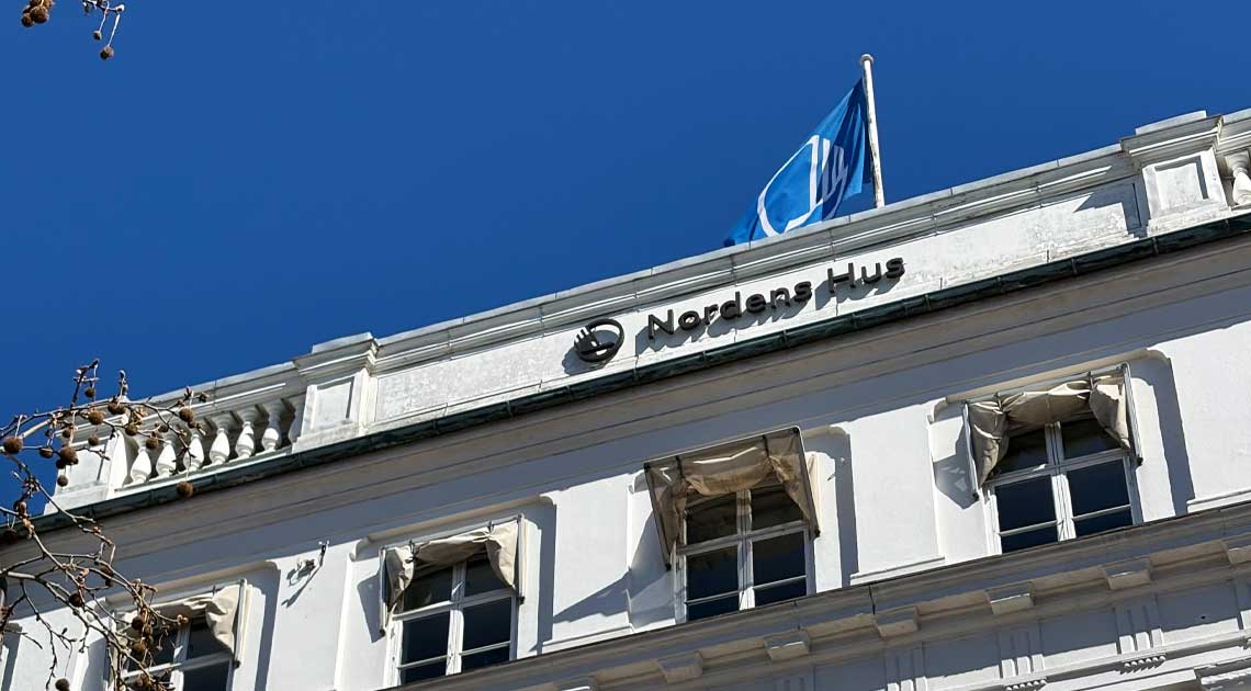 Facade of Nordens Hus with the Nordic Council flag waving under a clear blue sky.