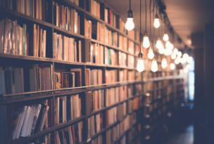 Bokhyllor fyllda med böcker i ett bibliotek, med hängande lampor längs gången.