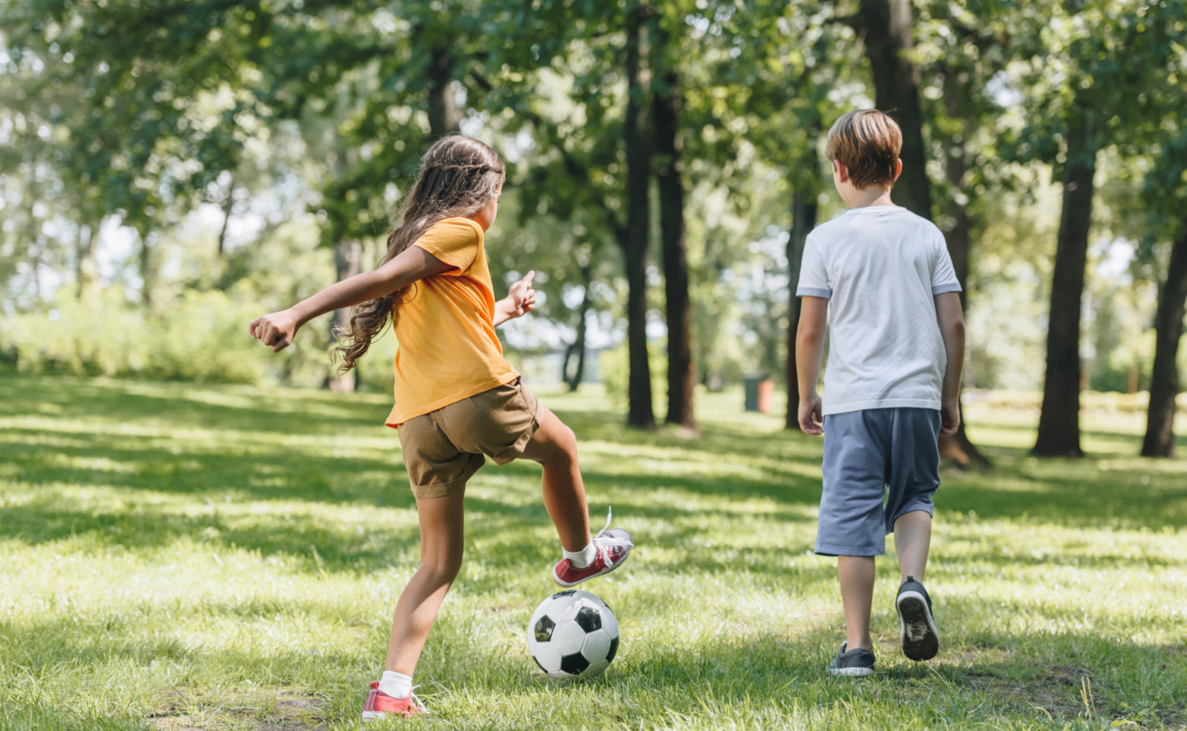 Back view of children playing soccer in a park.