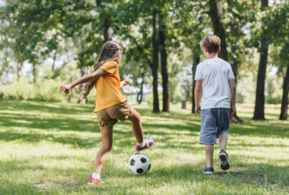 Back view of children playing soccer in a park.