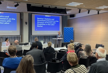 Woman giving a speech in a conference room. Text on powerpoint behind her: Seminar: Statistics and Quantitative Research on the Situation of Persons with Disabilities in the Labor Market