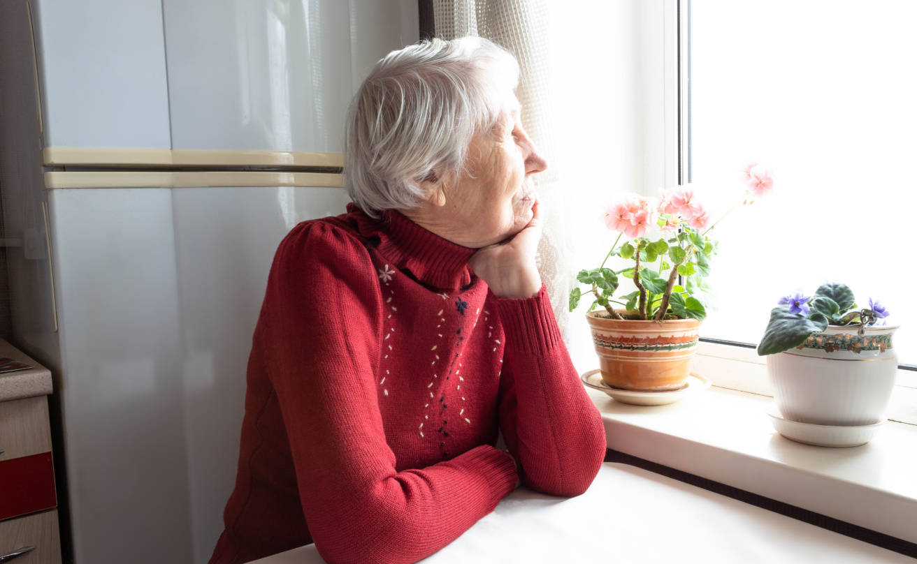 old woman sitting near a window in her house with red sweater