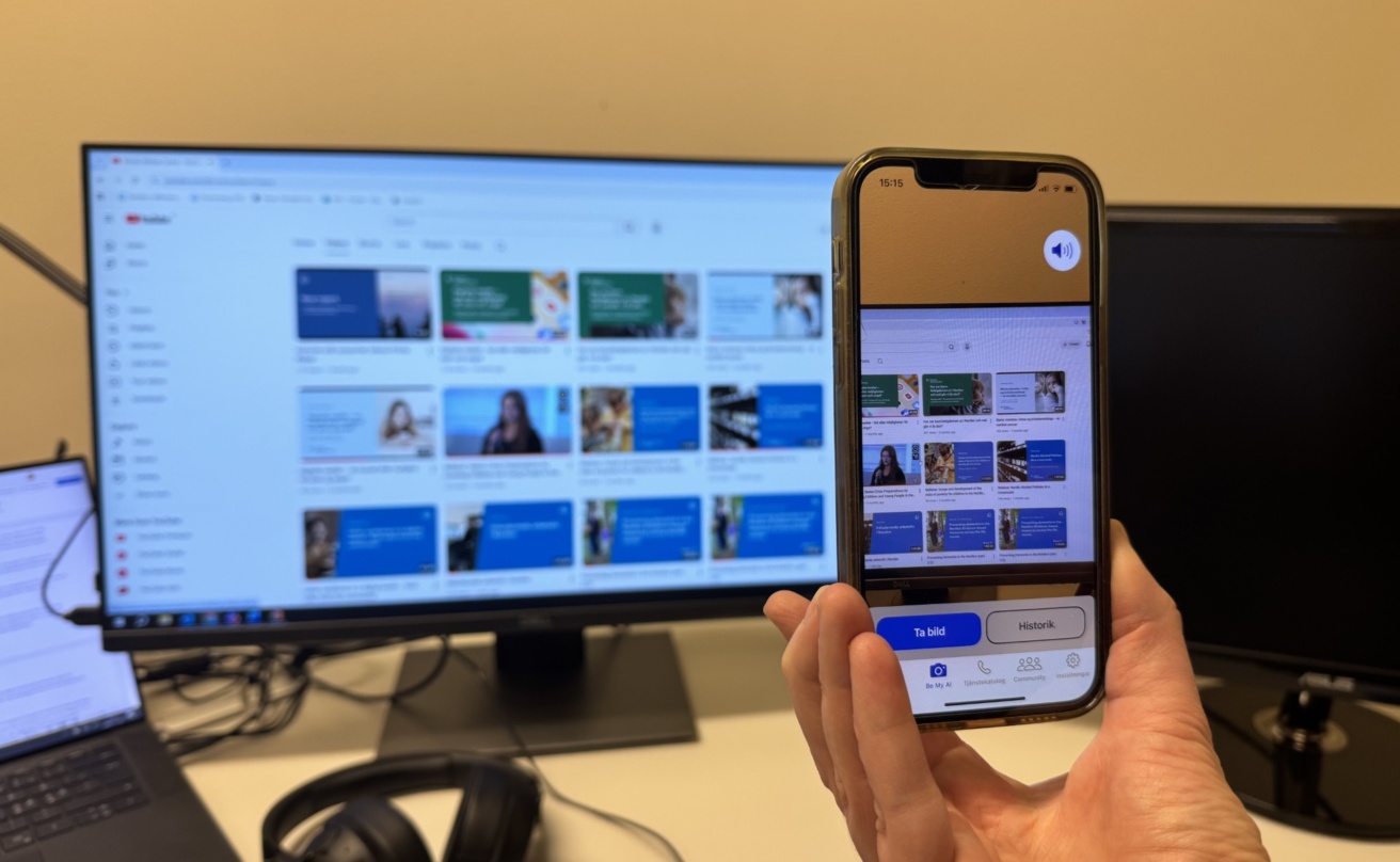 The app Be my Eyes poiting at a computer display with Youtube video thumbnails.