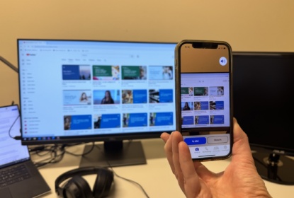 The app Be my Eyes poiting at a computer display with Youtube video thumbnails.
