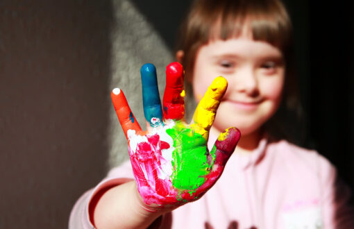 Flicka som håller fram en hand som är täckt med fingerfärg i olika kulörer.