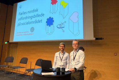 Två män står på scen i konferenslokal
