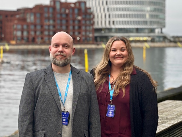 man and a woman standig with conference badges standing in front of urban landscape and water
