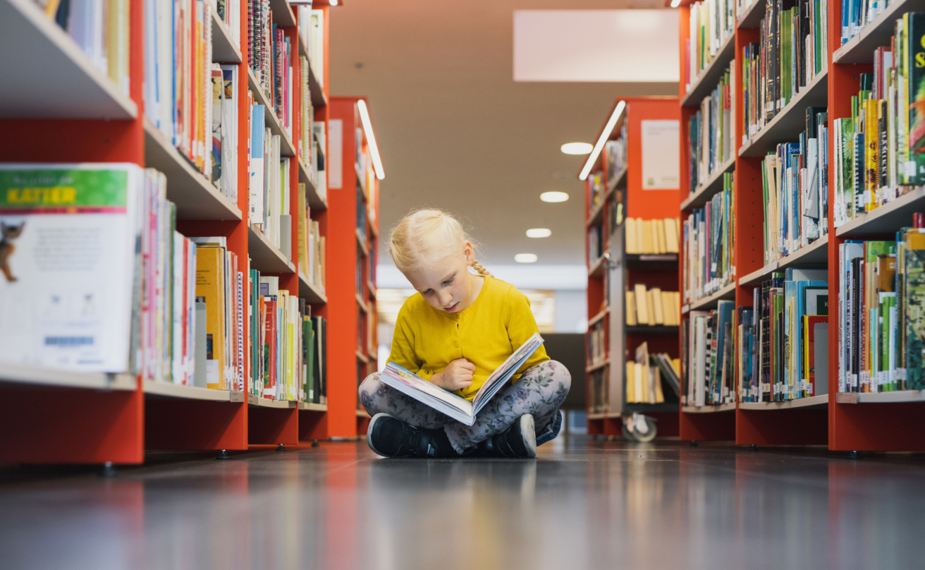 A child sitting on the library floor, reading