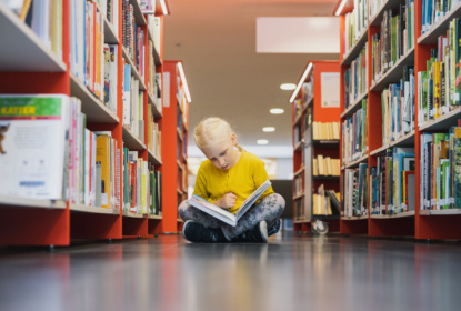 A child sitting on the library floor, reading