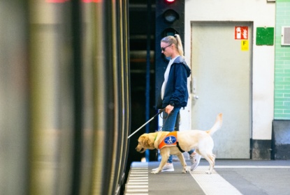 Synskadad kvinna med vit käpp och ledarhund stiger in i tunnelbanevagn