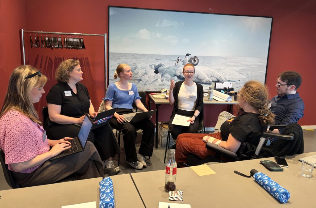 Sex personer sitter och diskuterar, en antecknar på dator
