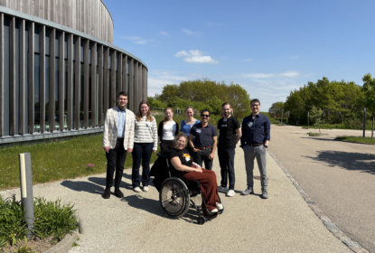 Gruppbild med 8 unga personer, varav en sitter i rullstol. De står utomhus i solen.