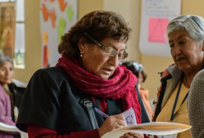 Two older women taking part in a group activity, with one writing notes on a sheet of paper.