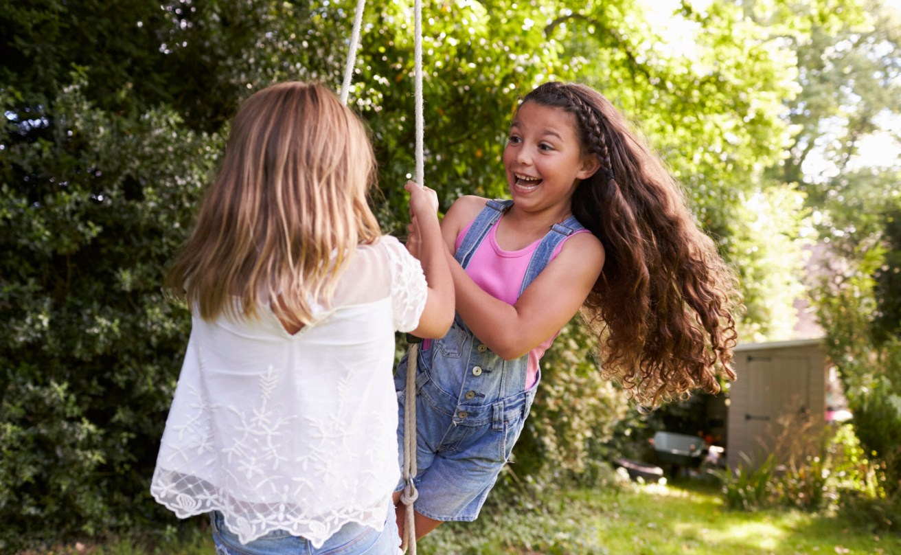 two girls playing together on tire swing in garden.