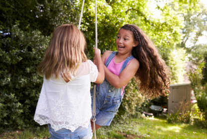 two girls playing together on tire swing in garden.